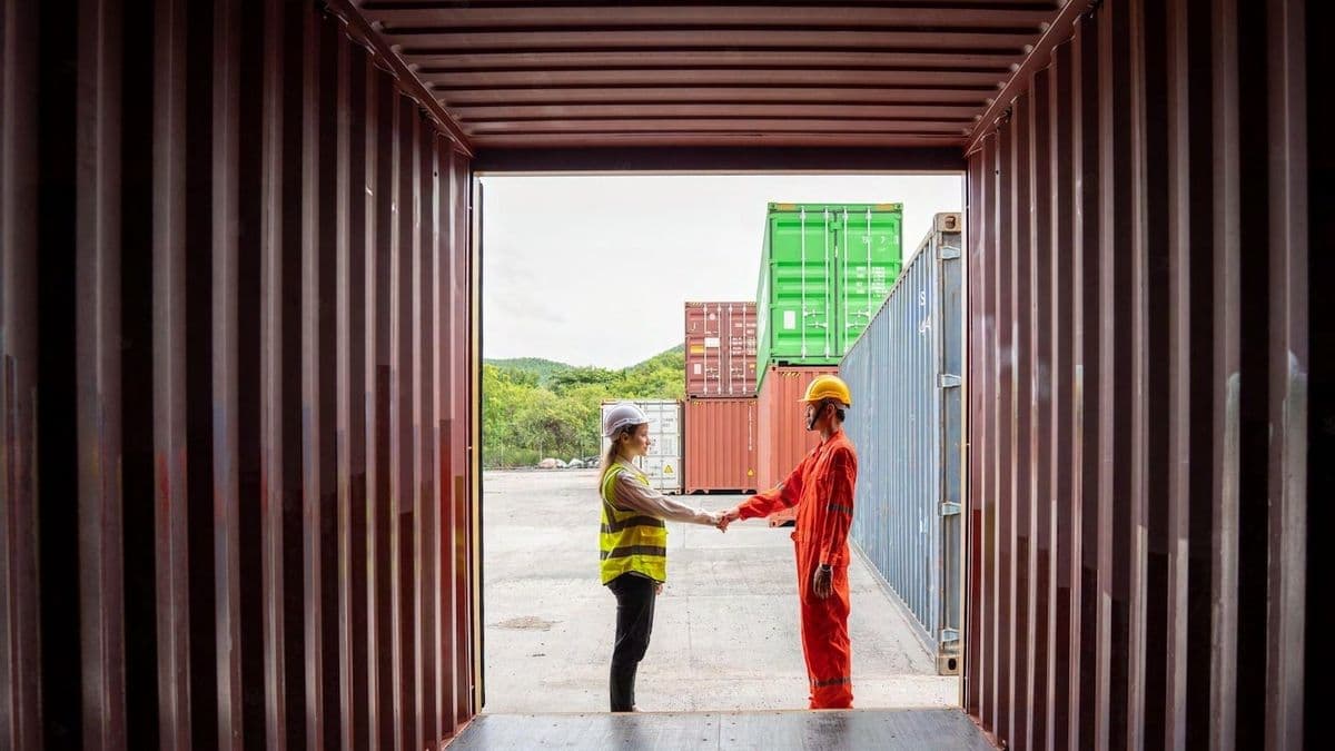 Dos trabajadores se dan la mano frente a un contenedor abierto